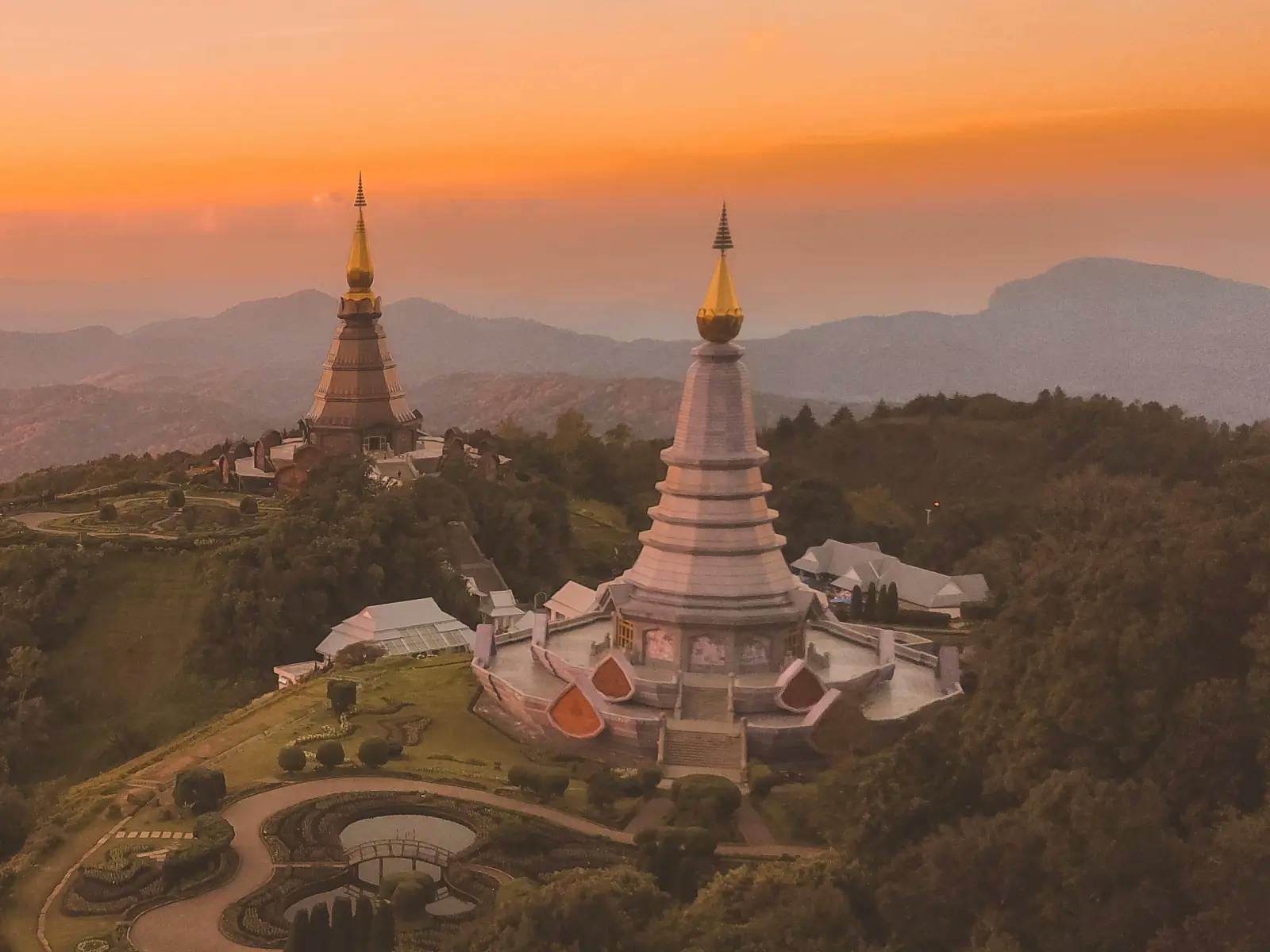 An aerial view of two golden pagodas on top of a hill with a beautiful sunset in the background. The pagodas are located in Doi Inthanon National Park, Thailand.