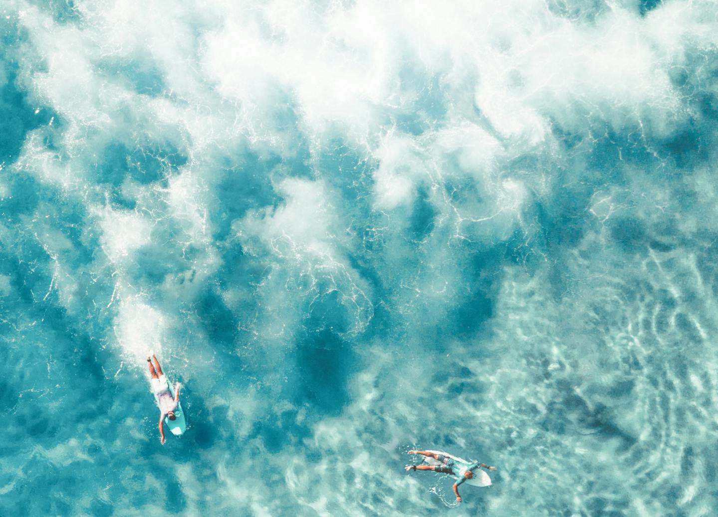 a birds-eye view of surfers paddling around crystal clear water