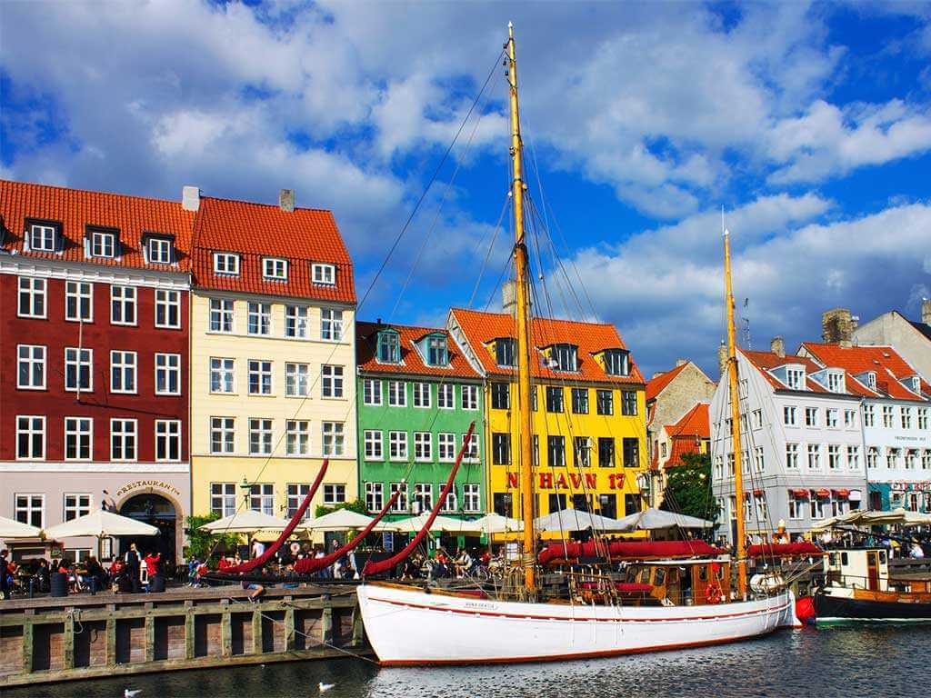 White sailboat in the harbor in Copenhagen with colorful buildings in the background