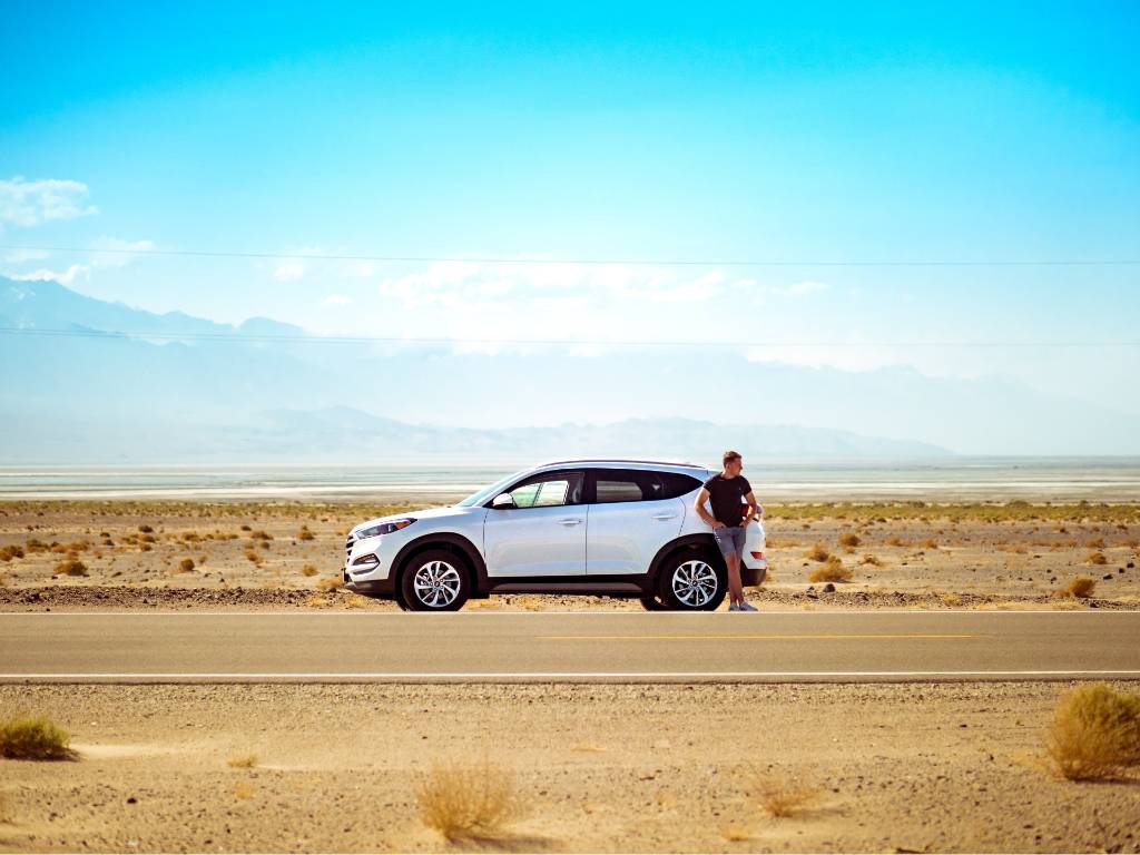 car on the side of the road with driver standing by door.