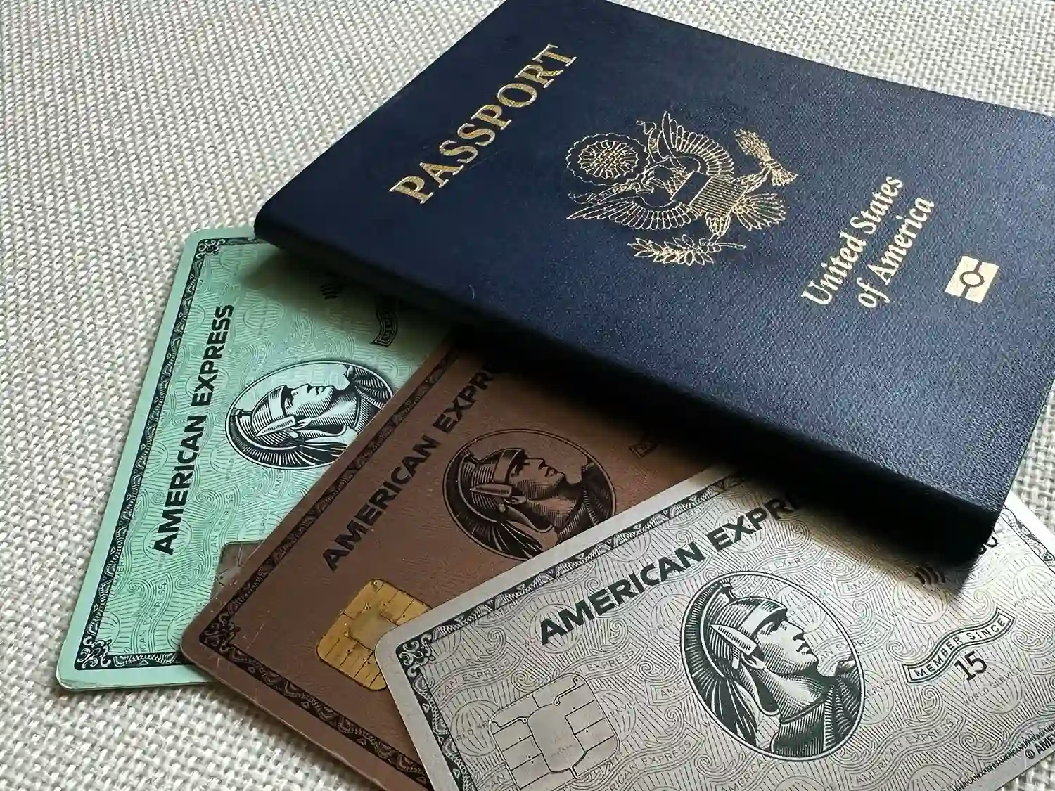 Three cards from American Express — the Green Card, the Gold Card, and the Platinum Card — peeking out from underneath a US passport
