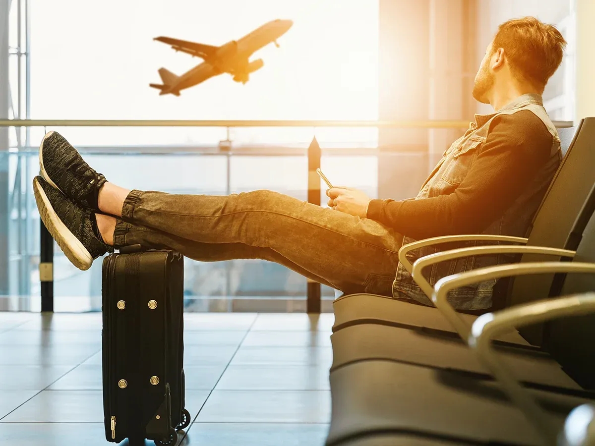 A photograph of a person sitting in an airport terminal watching a plane takeoff