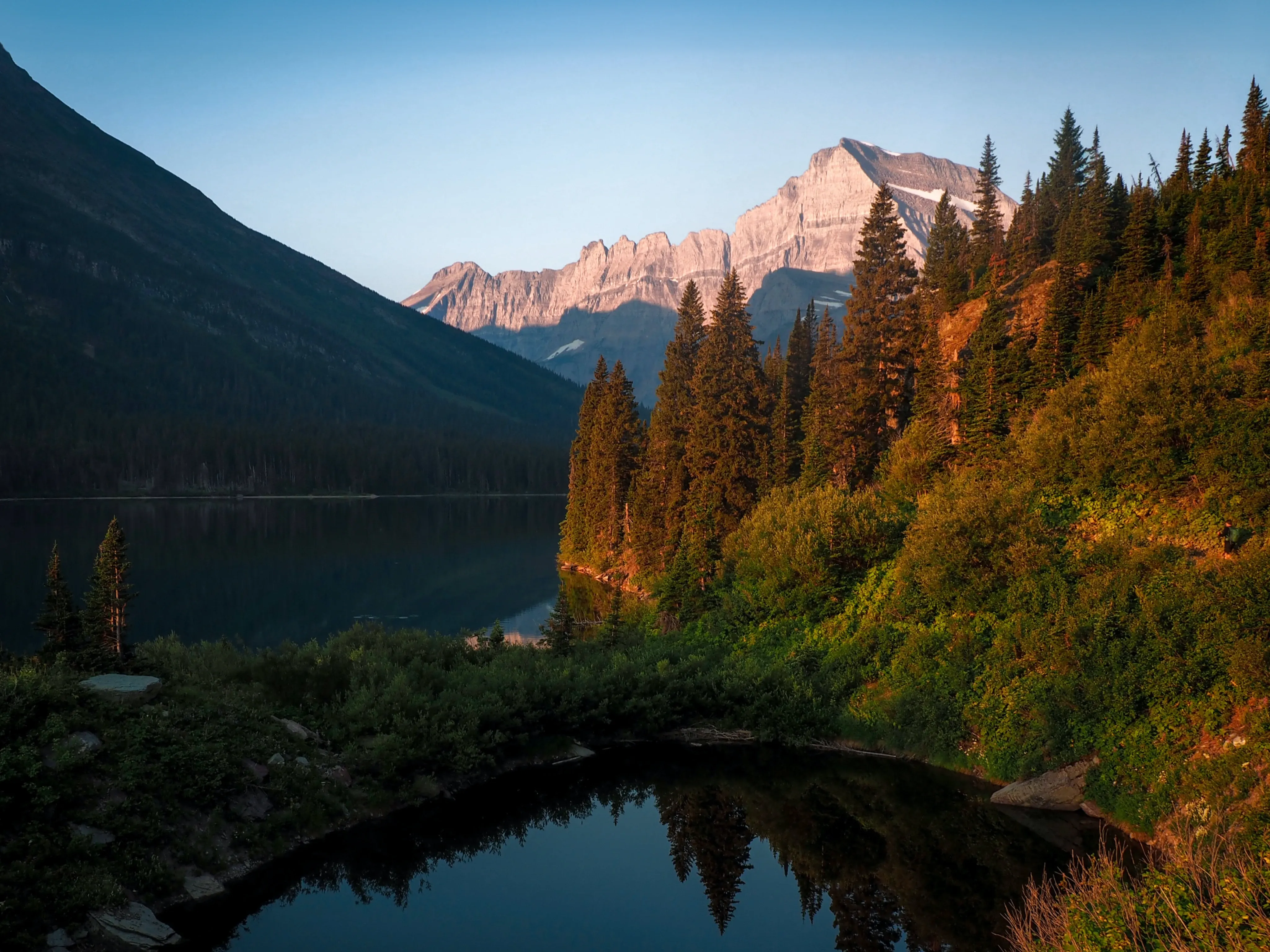 A lake sits in front of a sunlit mountain in rural Montana