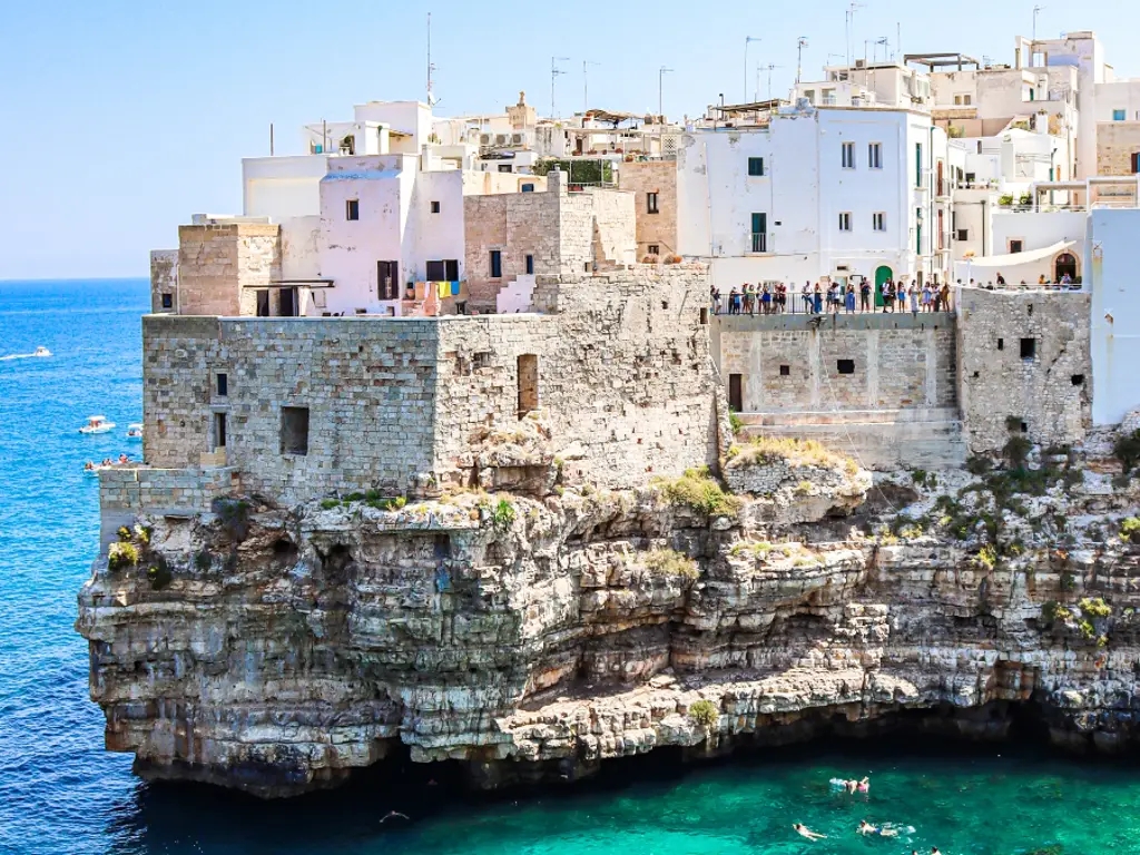 A rock piled high with white-washed buildings juts out into the blue water in Puglia