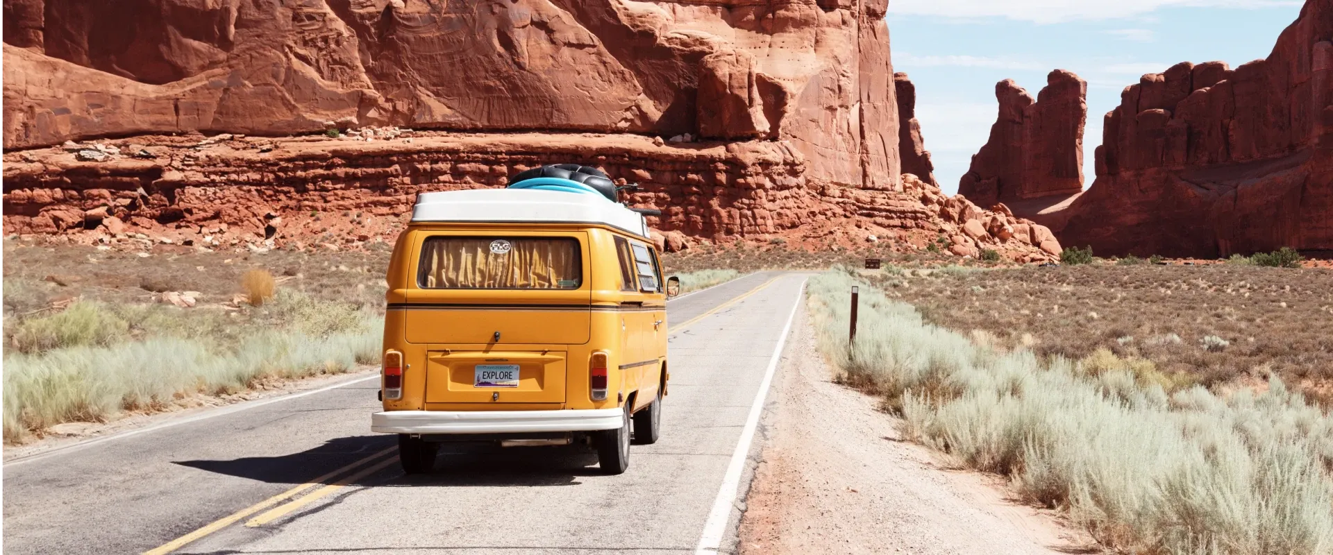A yellow van drives through red rocks at a national park