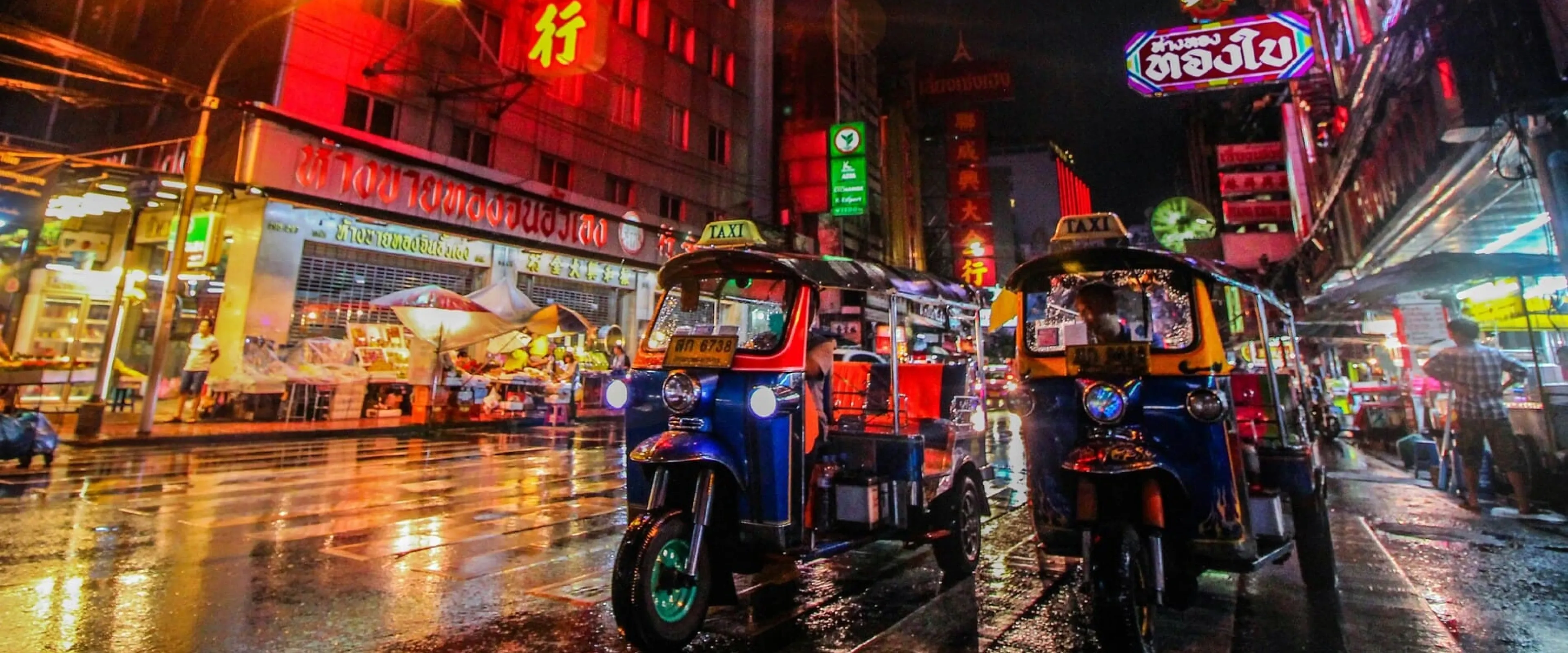 Tuk tuks drive down a busy, lit road in Bangkok