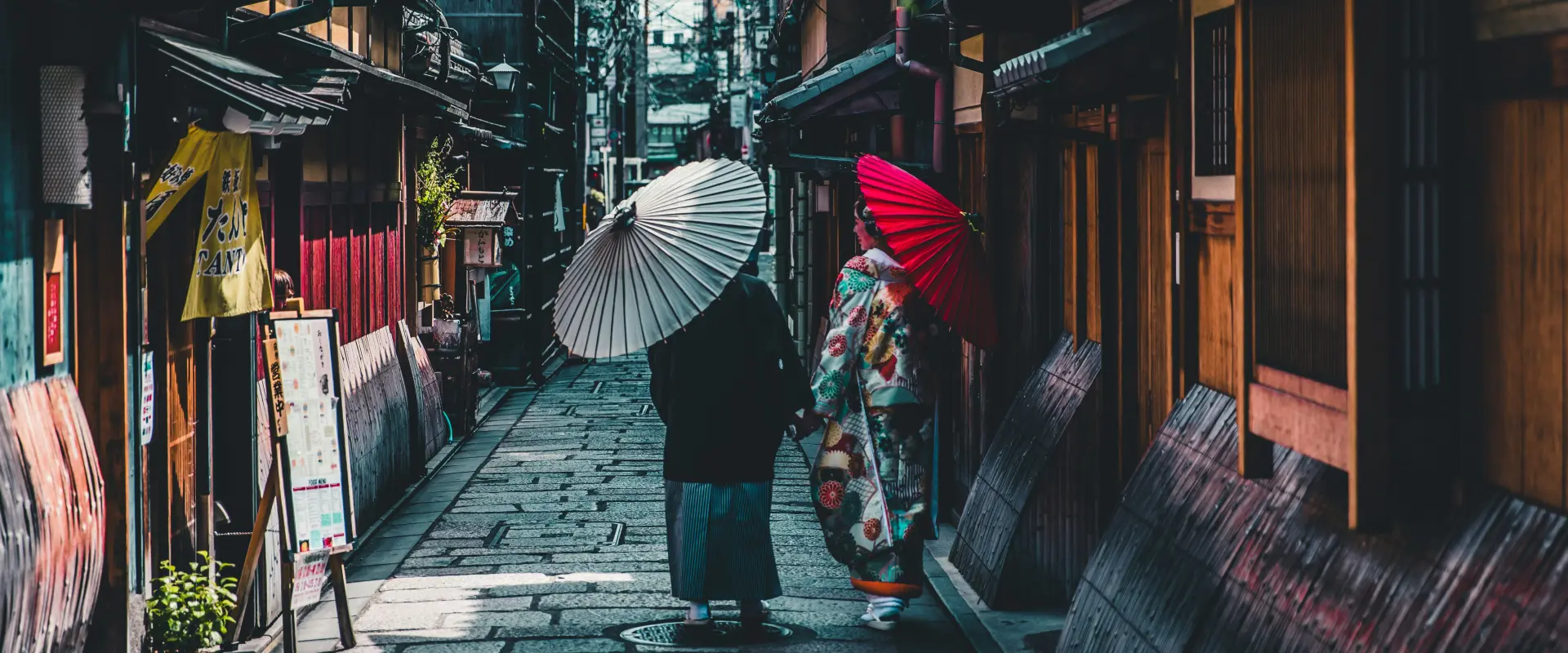Women with umbrellas walk down an alley in Asia