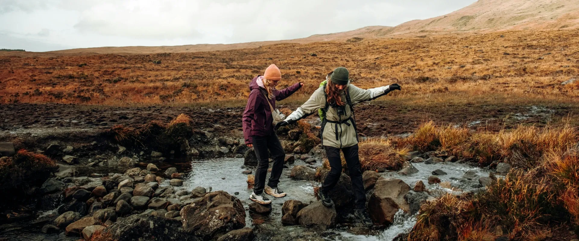 Two people stepping on rocks across a river