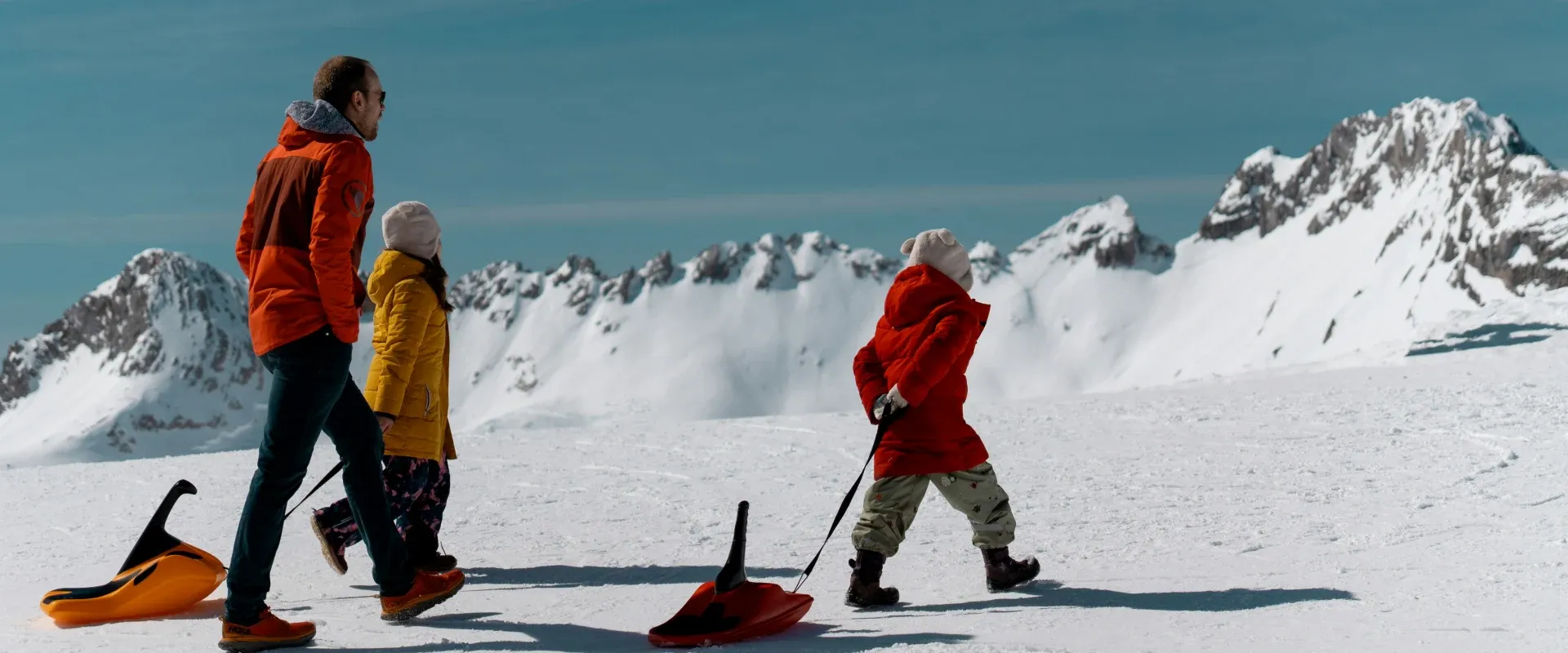 Family with kids pull sleds up snowy mountain