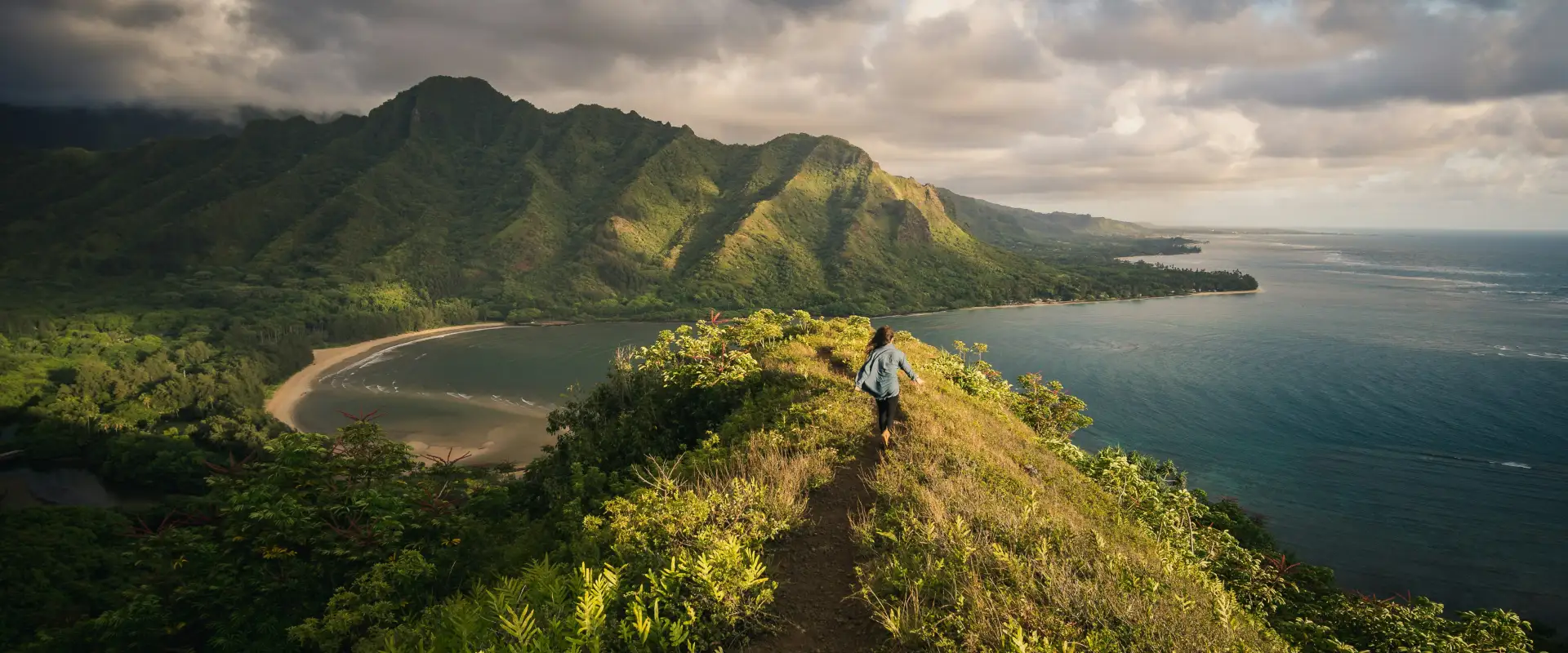 Woman stands on hill overlooking coastline of Hawaii