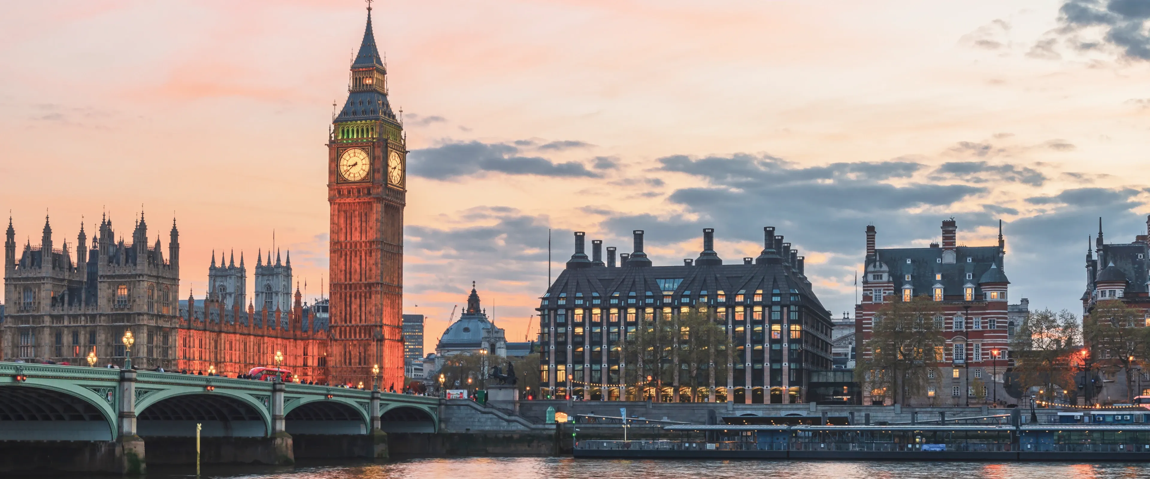 Big Ben sits on the Thames River in London at sunset