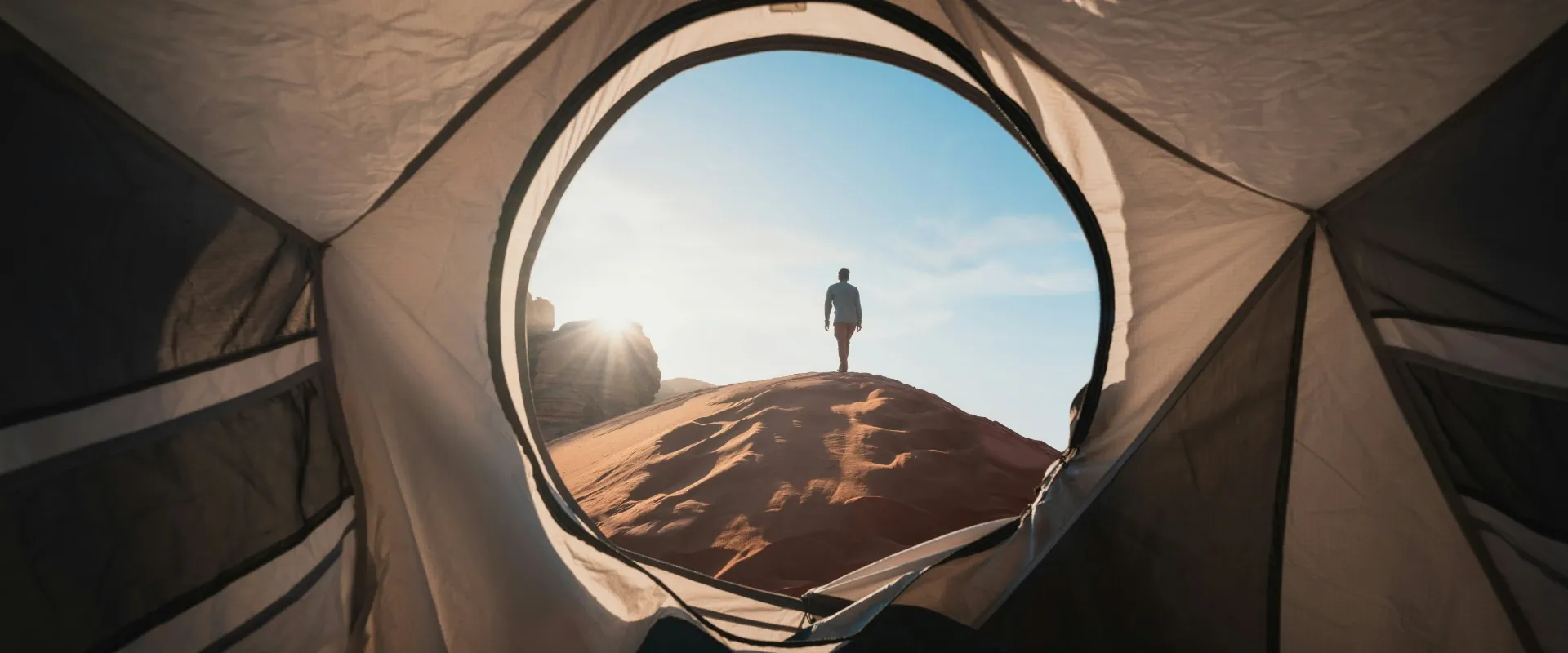 View of man climbing sand dunes from the inside of a tent