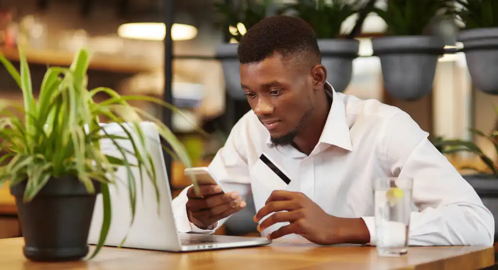 man holding phone and credit card in front of laptop